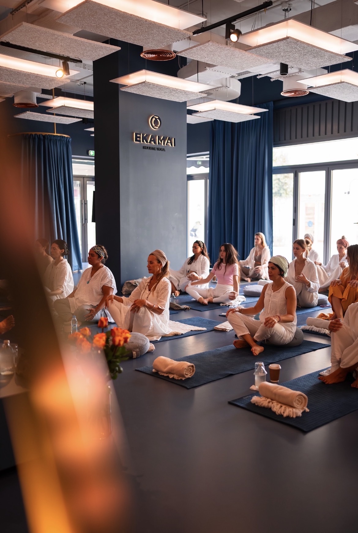 A group meditating beneath illuminated ceiling panels inside the Eka Mai Dubai studio