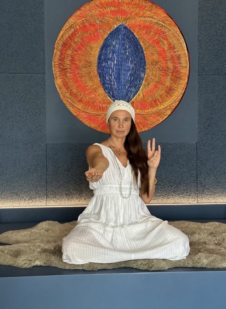 A woman seated in meditation before circular wall artwork